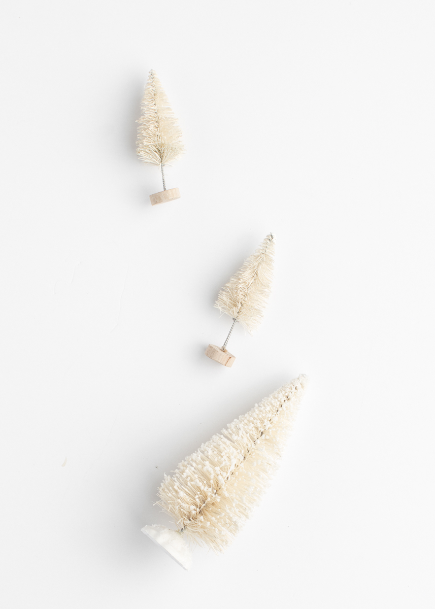A minimalistic holiday flat lay featuring three cream bottlebrush trees arranged in a diagonal in Tulsa Christmas events and studio setups.