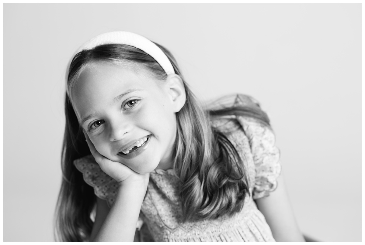 Black and white portrait of a young girl resting her head on her hand, showing a genuine smile during a relaxed family photos Tulsa session.