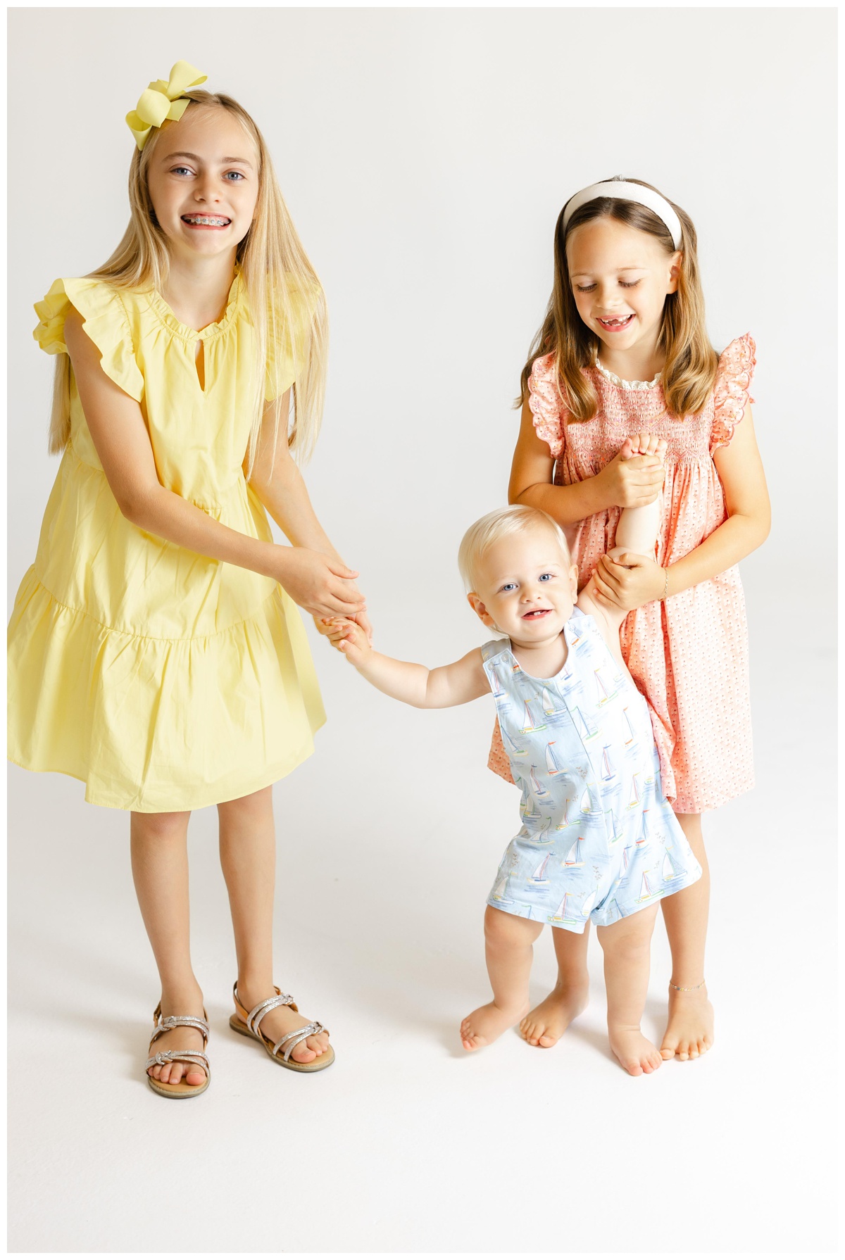 Three siblings playing and holding hands during a joyful moment in the studio, captured during a vibrant and playful family photos Tulsa session.