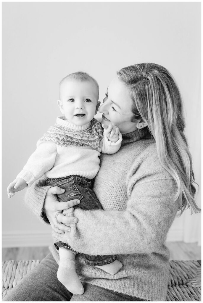 A sweet black-and-white photograph of a mother holding her smiling baby during their family portraits.a