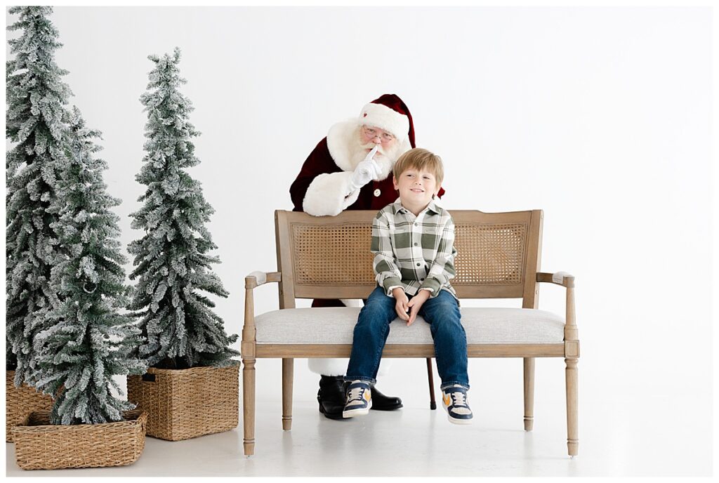 Young boy smiling as Santa surprises him from behind during Christmas pictures