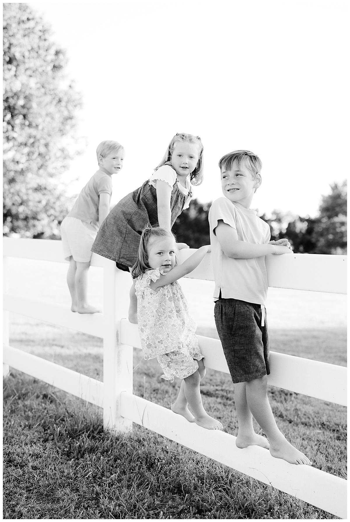 Four young siblings playing together on a white fence during an outdoor family photography session